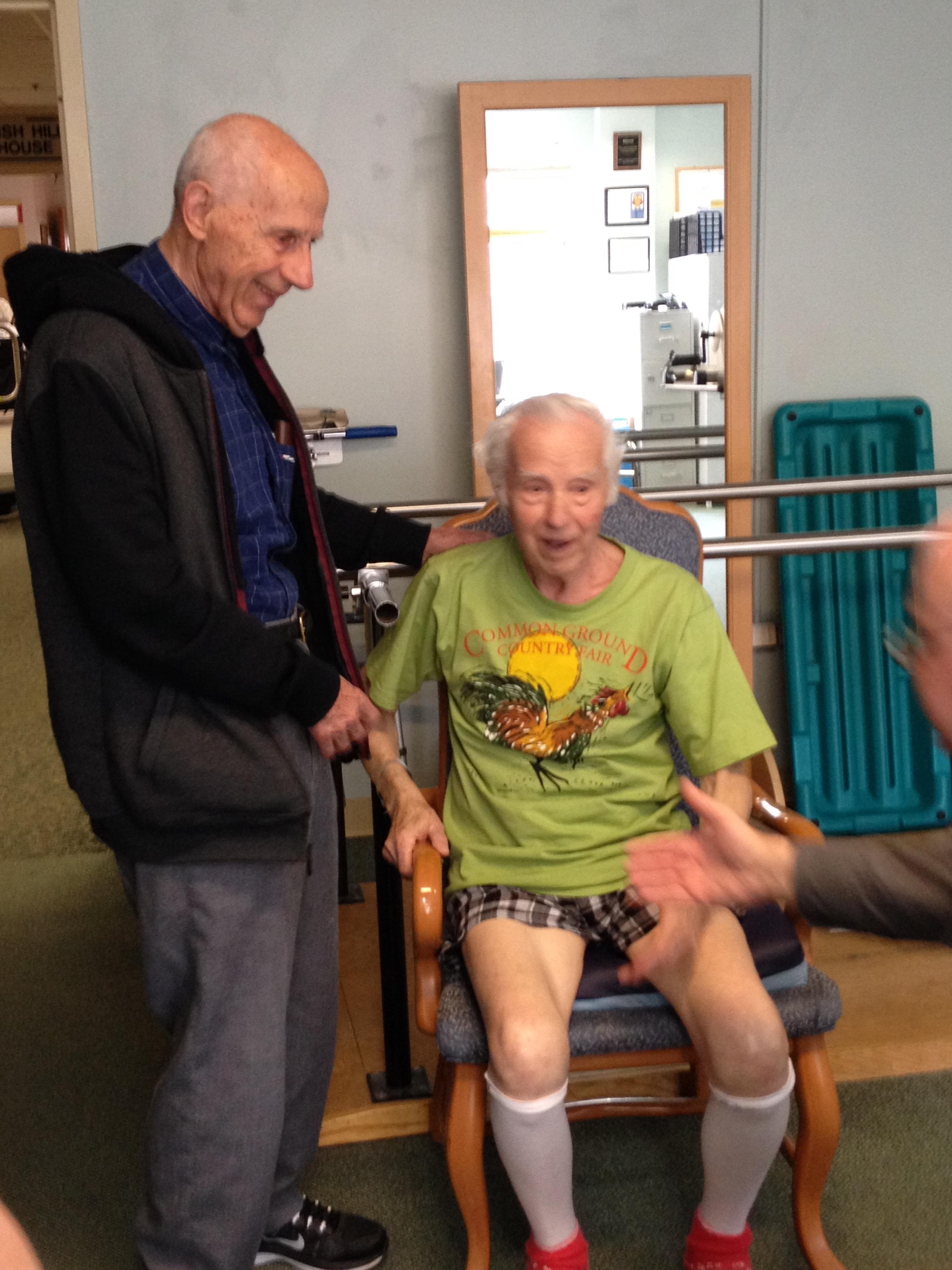 A man standing next to an older man in a chair