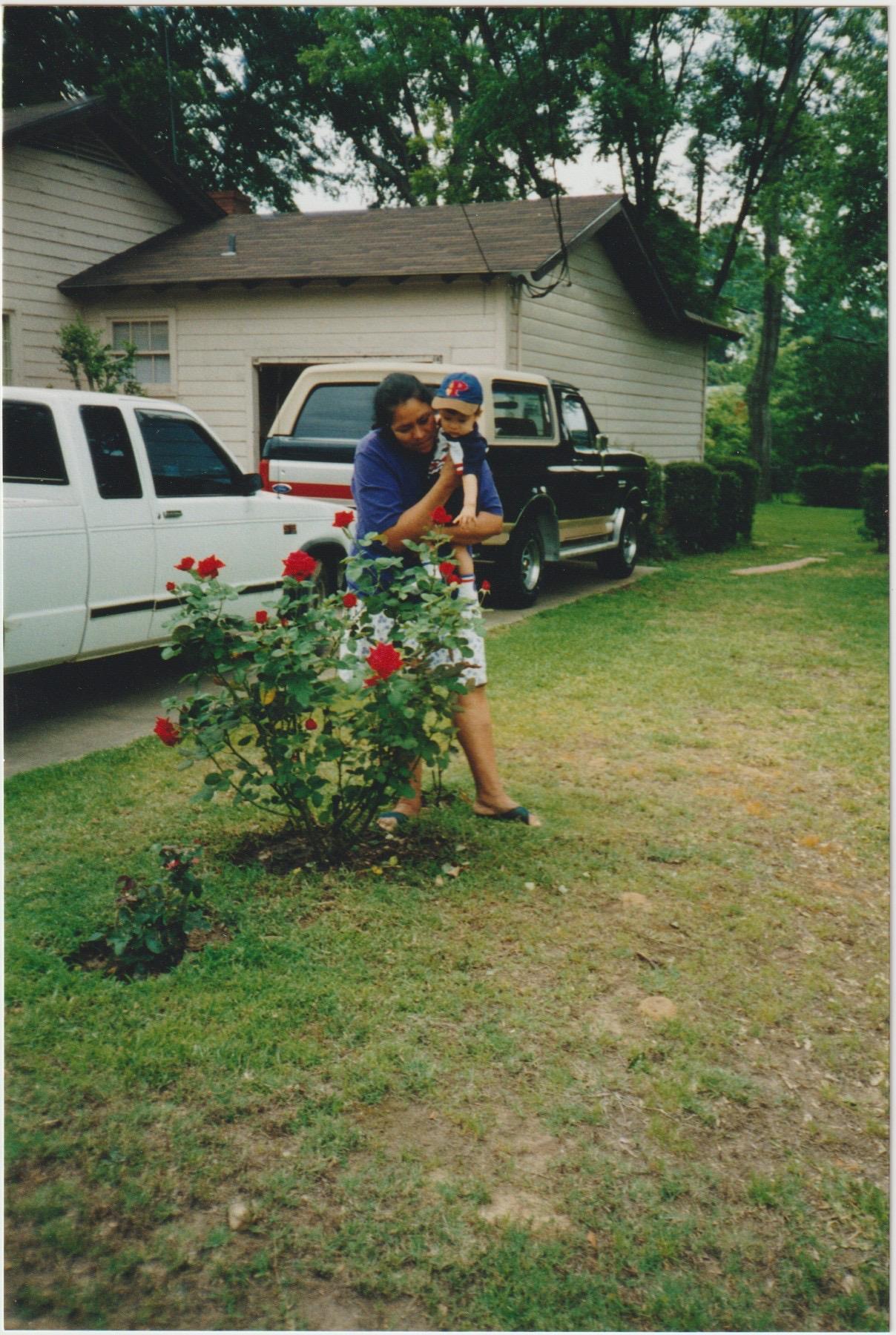 A woman holding a child in front of a rose bush