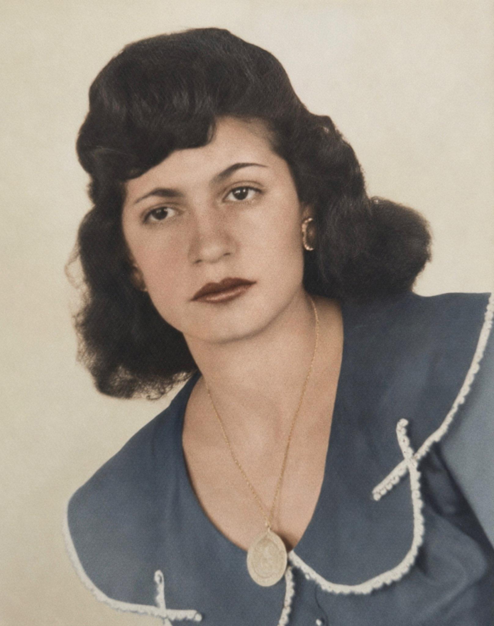 A woman with dark hair wearing a blue shirt and a gold necklace