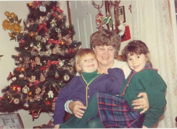 A woman holding two children in front of a christmas tree