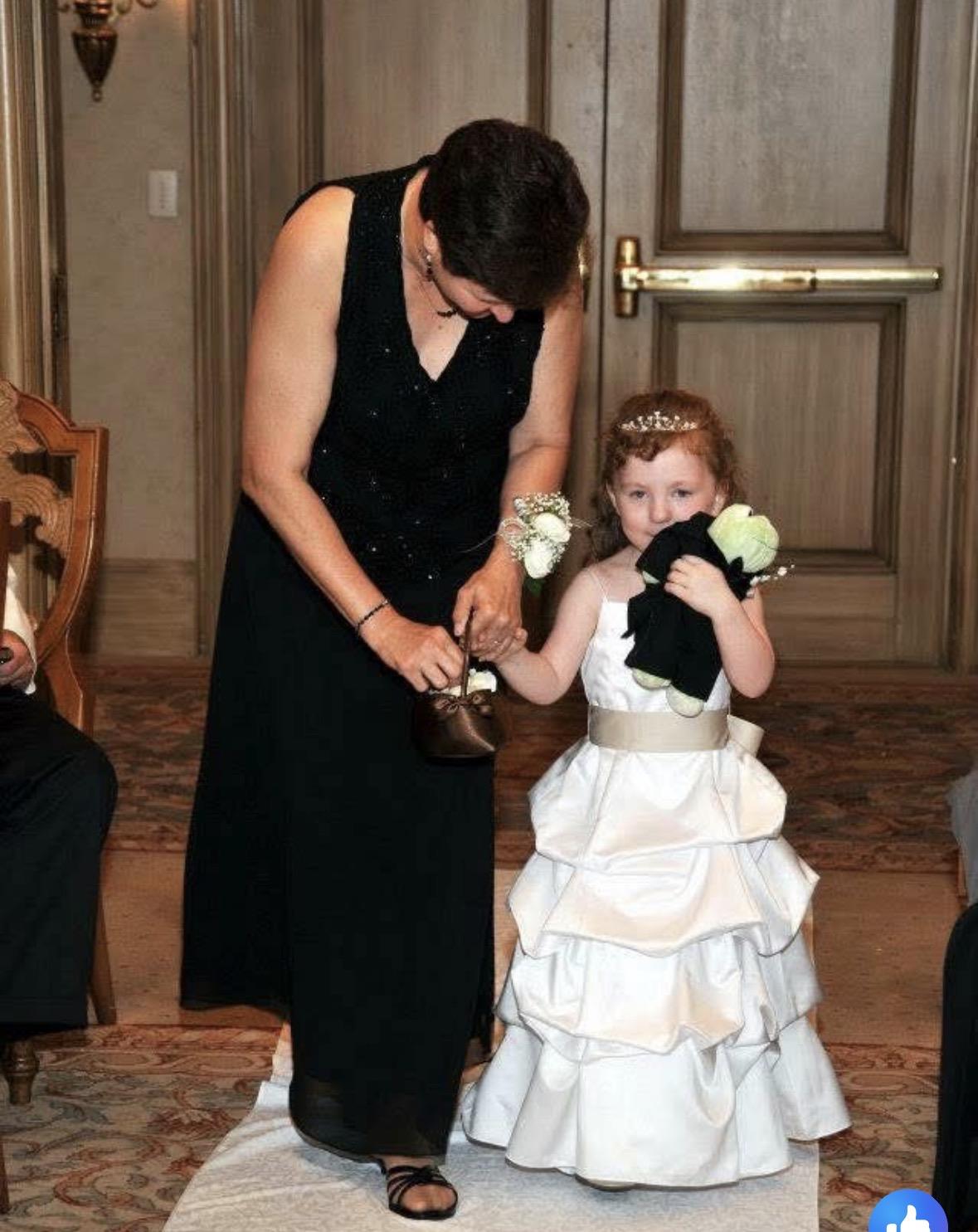 A woman in a black dress holding a flower girl's shoes