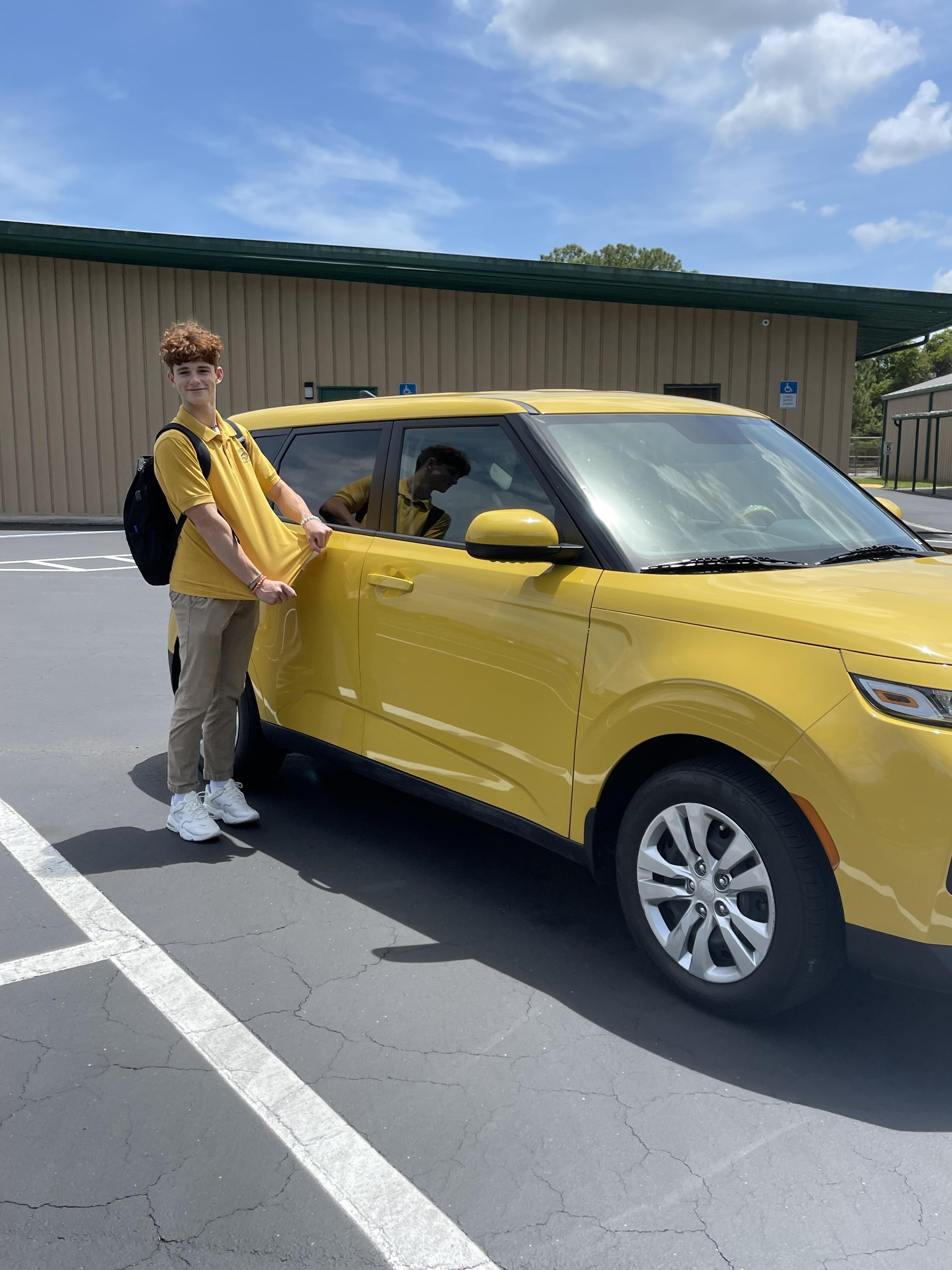 A boy standing next to a yellow car
