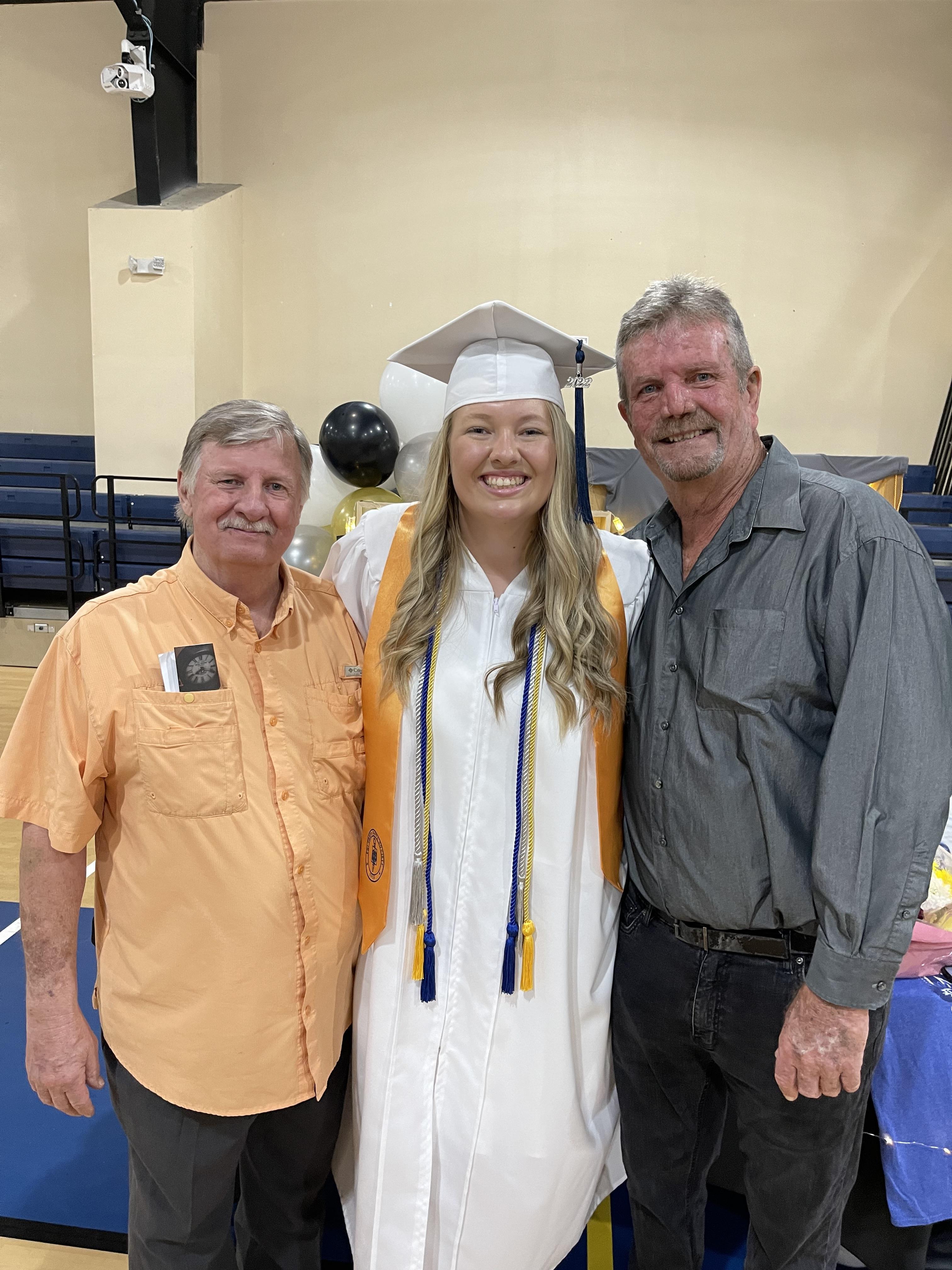 A woman in a graduation cap and gown with a man in a room with balloons