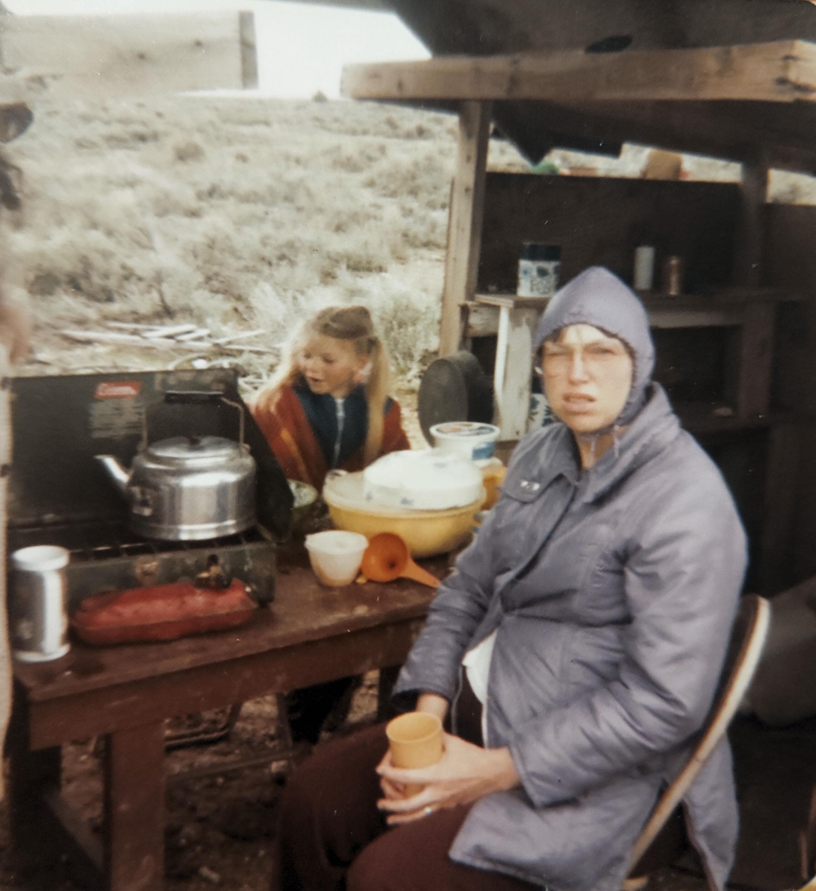 A woman sitting at a table with a girl in the background
