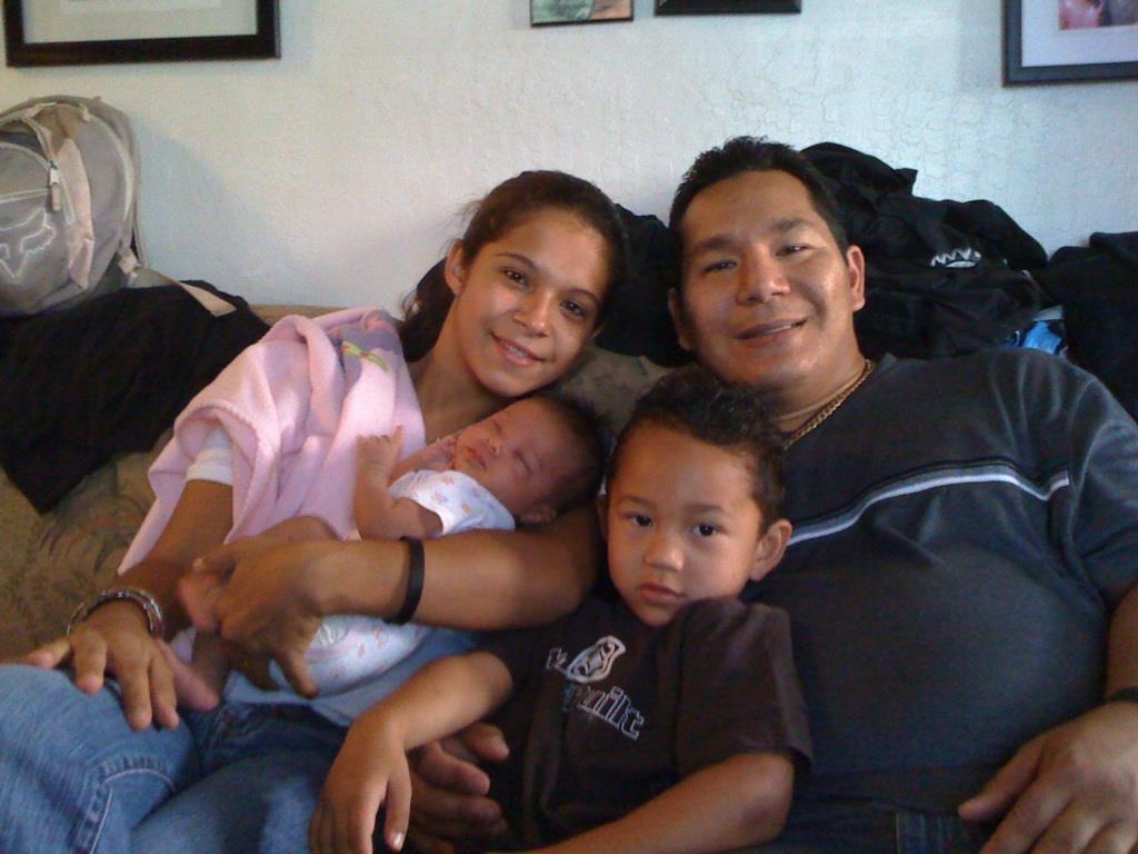 A family sits closely together, with a newborn in the mother's arms and a young boy beside them.