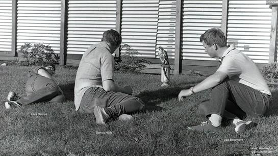 Three friends enjoy the sunshine on the grass, playing with a small statue.